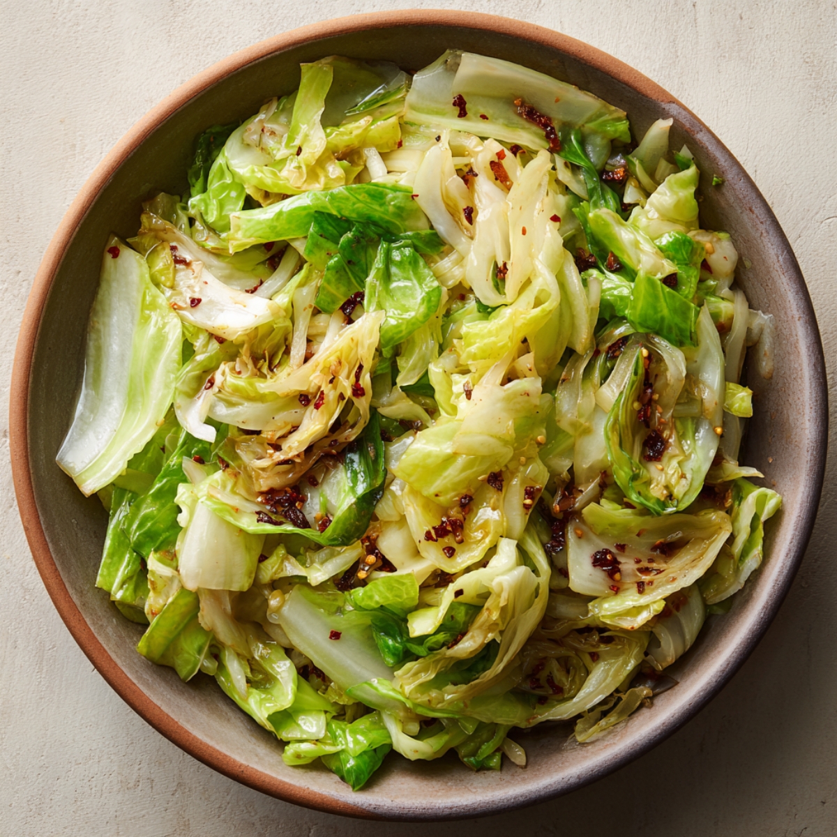 bowl of cabbage stir-fry with red chili flakes sprinkled on top.