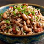 bowl of black-eyed peas and rice, hoppin john recipe garnished with chopped cilantro and green onions. The dish looks colorful, with red peppers and the rice and beans mixture well-combined.