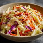 Creamy coleslaw recipe e in a rustic bowl, made with shredded green and red cabbage and carrots tossed in a tangy mayonnaise dressing.
