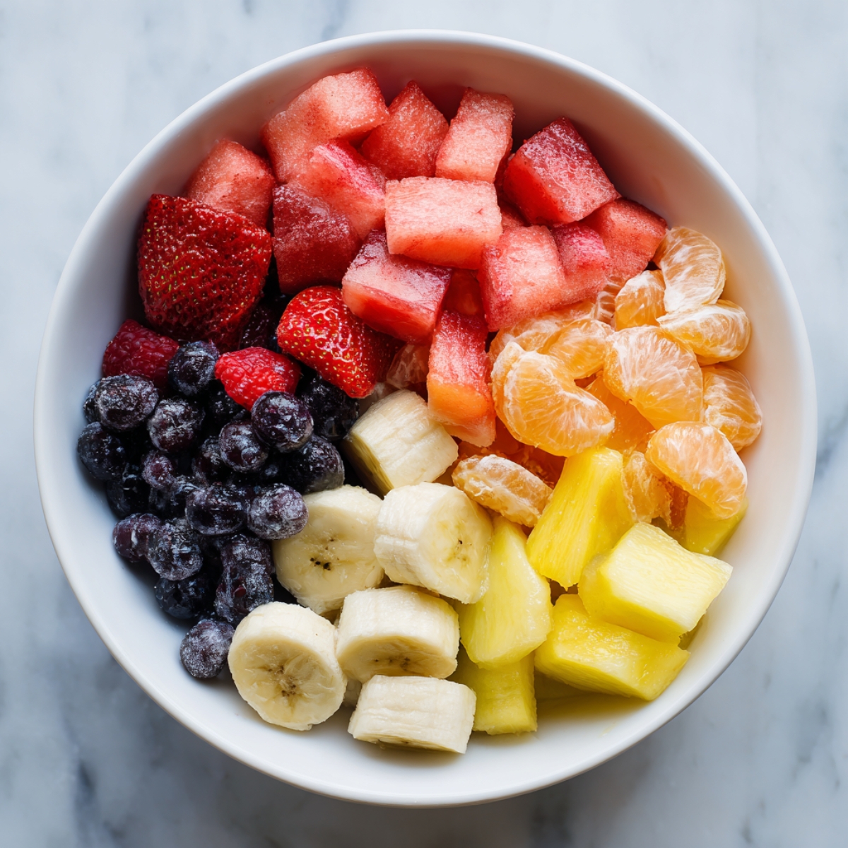A fresh fruit salad in a ceramic bowl with strawberries, bananas, blueberries, and pineapple drizzled with honey and garnished with mint leaves.