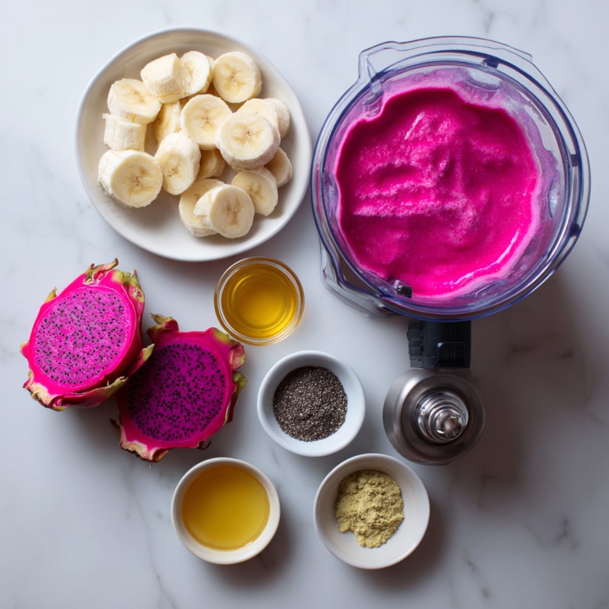 top-down view of sliced bananas, frozen dragon fruit, chia seeds, and oil, with a blender filled with blended dragon fruit smoothie