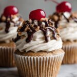 Close-up of a homemade cupcake recipes topped with swirls of frosting, chocolate drizzle, and a cherry on top