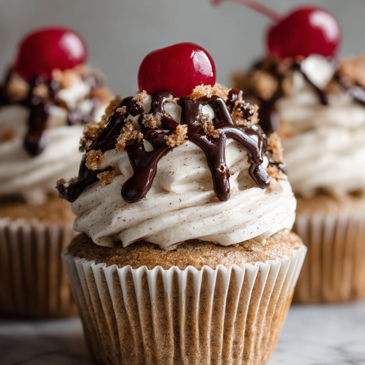 Close-up of a homemade cupcake recipes topped with swirls of frosting, chocolate drizzle, and a cherry on top