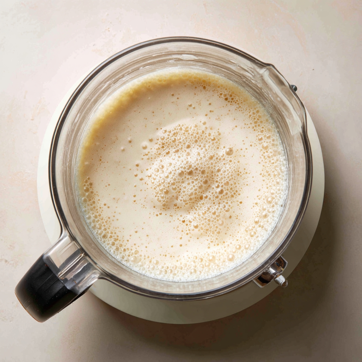 top-down view of a blender with frothy milk or cream inside, likely being prepared for a coffee or dessert drink