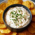 creamy onion dip recipe garnished with fresh chives and served with a side of crispy potato chips.