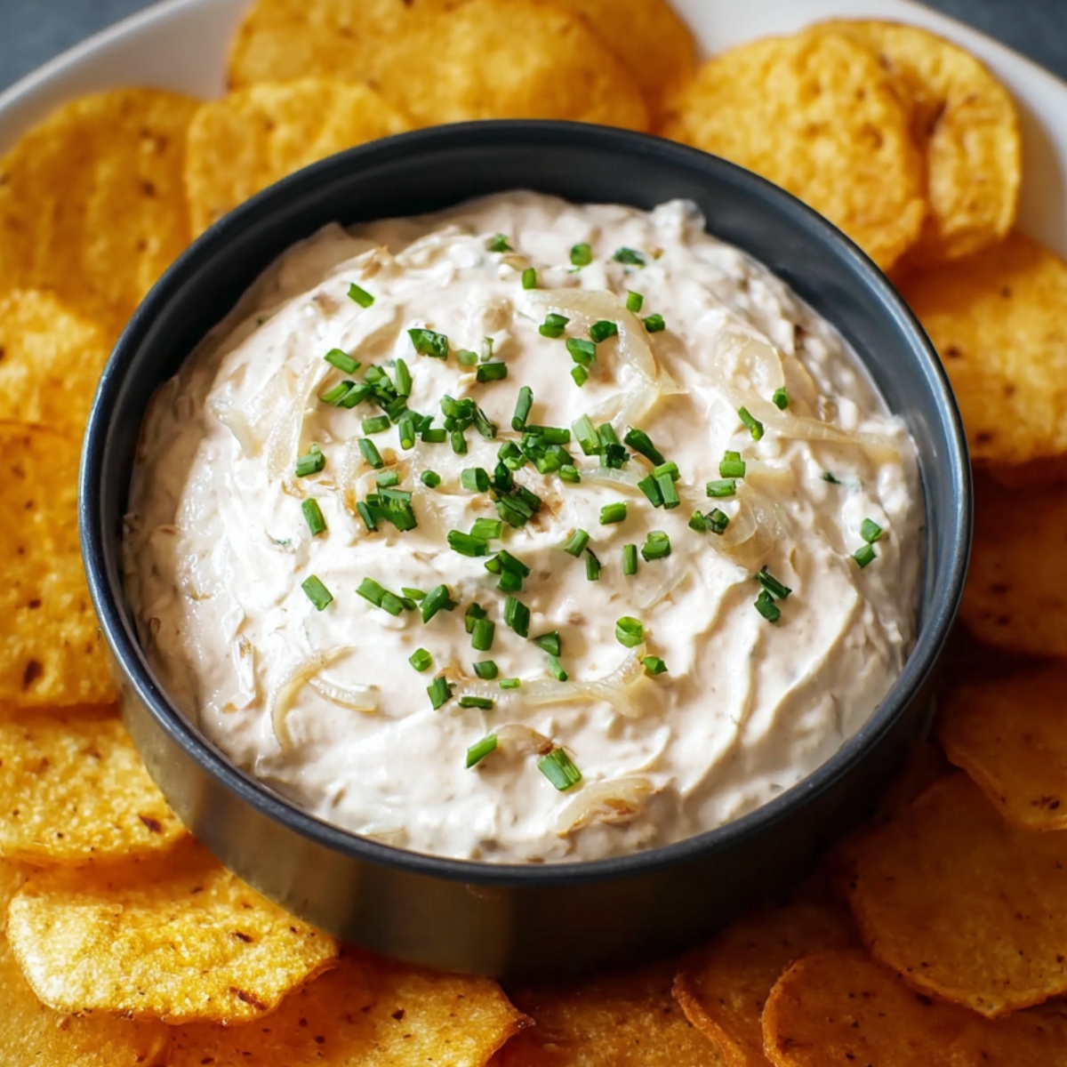 creamy onion dip recipe garnished with fresh chives and served with a side of crispy potato chips.
