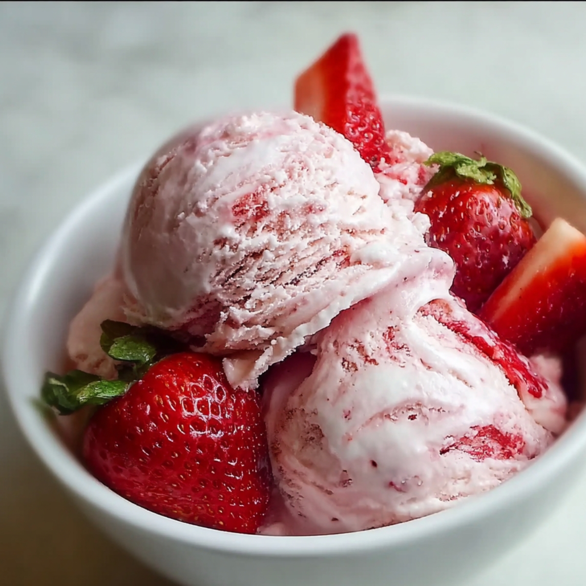 bowl of strawberry ice cream recipe with fresh whole strawberries on top, in a white bowl.