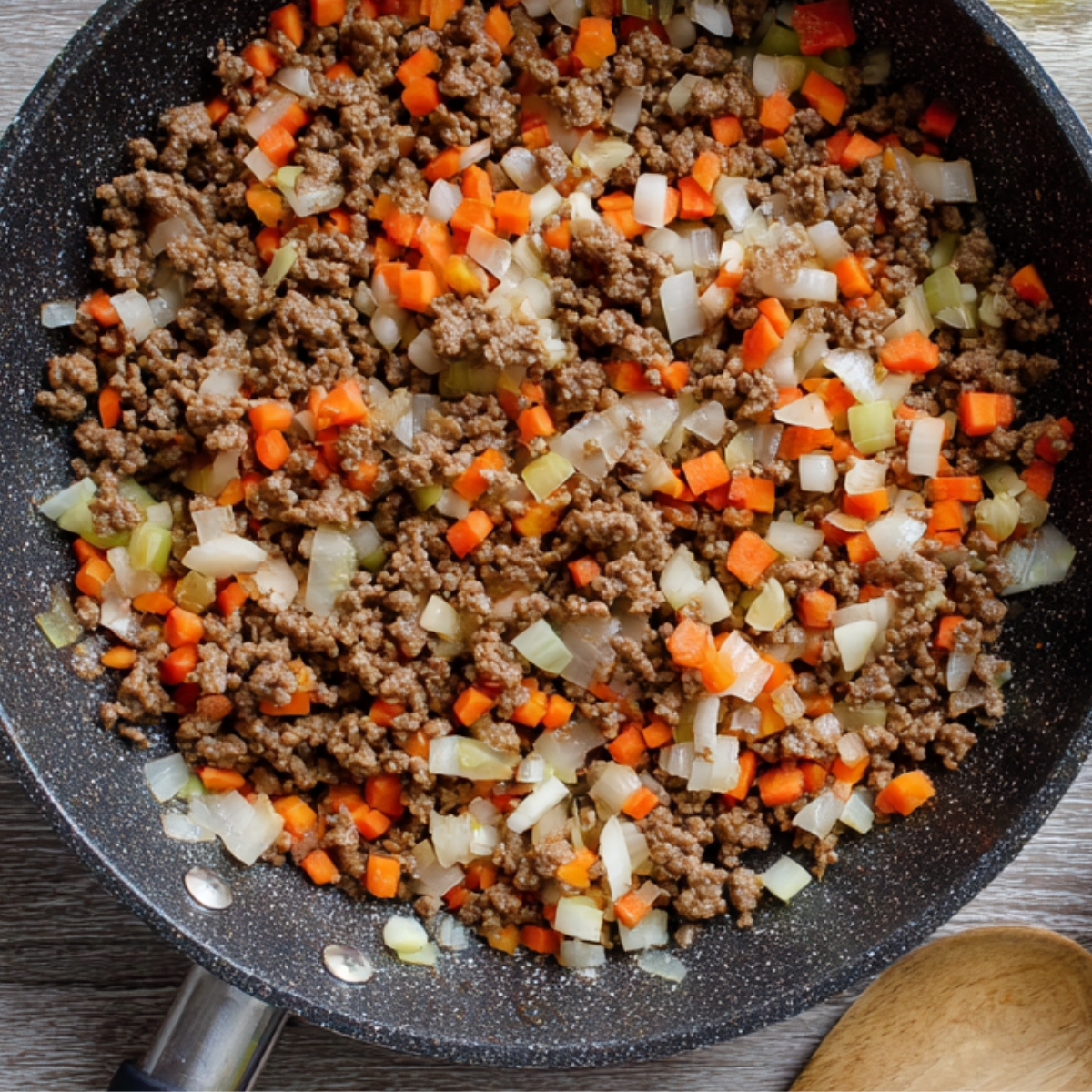 skillet with ground beef, carrots, and onions being sautéed together, with the vegetables finely chopped and mixed with the meat