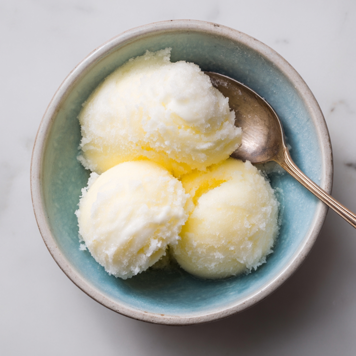 small bowl containing three scoops of lemon sorbet, with a spoon resting beside it.