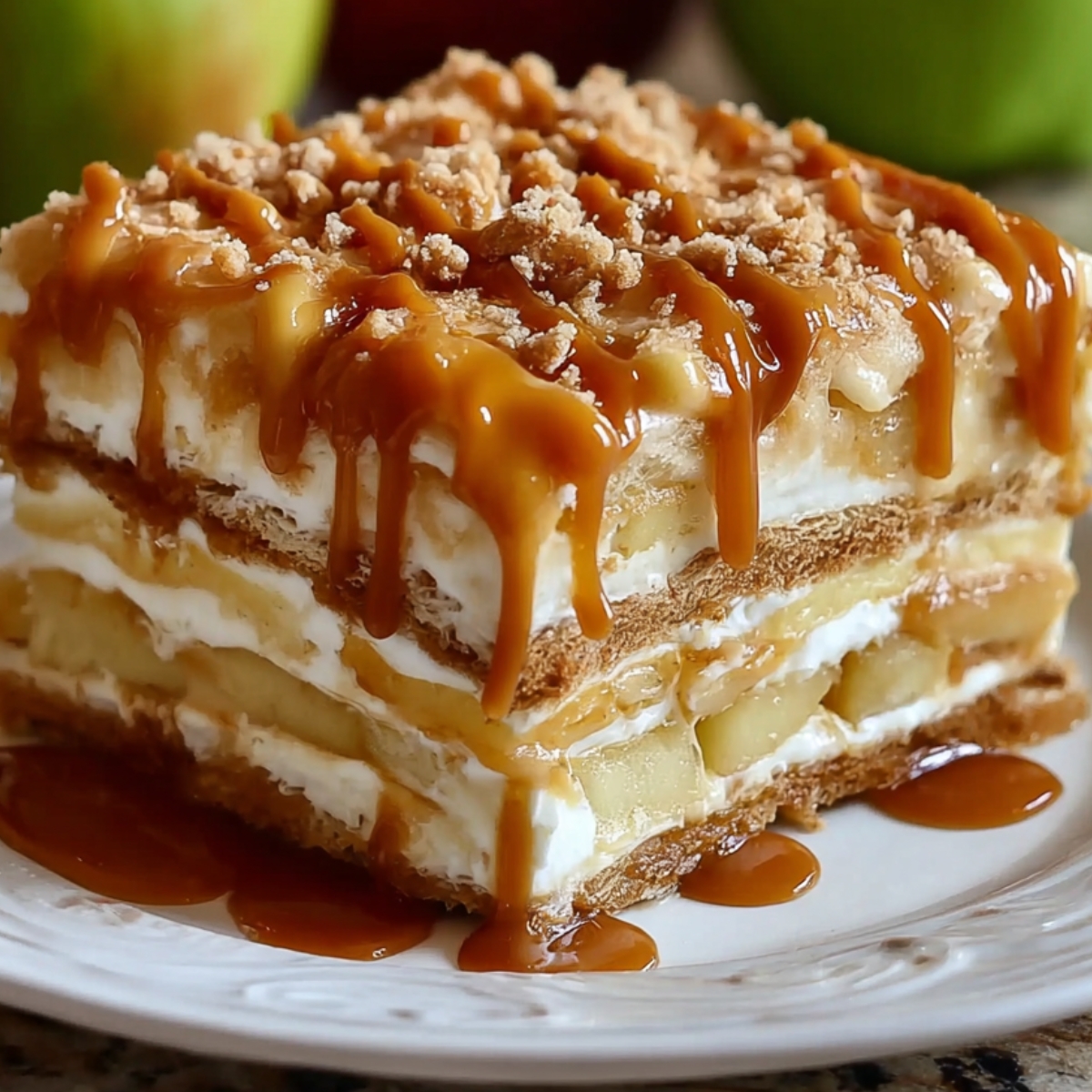 delicious layered dessert Caramel Apple Eclair Cake , whipped cream, apple slices, and caramel sauce drizzled on top. The dessert is garnished with crumbled bits on top, likely from the graham crackers or other ingredients