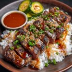 A close-up of a dish featuring slices of hibachi steak atop a bed of rice. The steak is garnished with sesame seeds and green onions, and a side of pickled cucumbers. There’s a small bowl of sauce next to the plate.