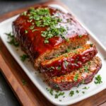 Juicy sliced easy meatloaf recipe on a white platter topped with shiny glaze and sprinkled with fresh parsley.