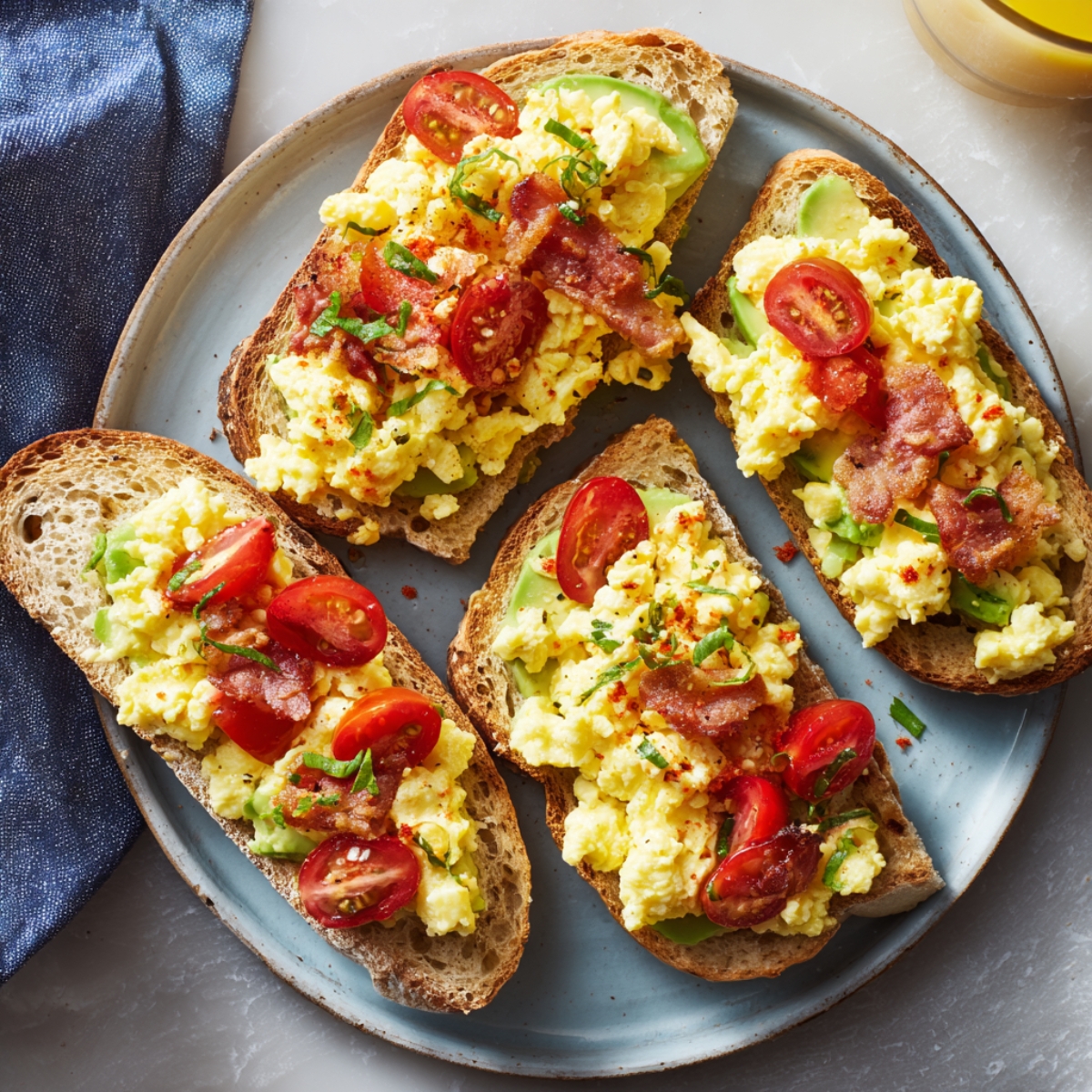 Breakfast bruschetta with creamy scrambled eggs, crispy bacon, avocado, and cherry tomatoes served on toasted sourdough slices.