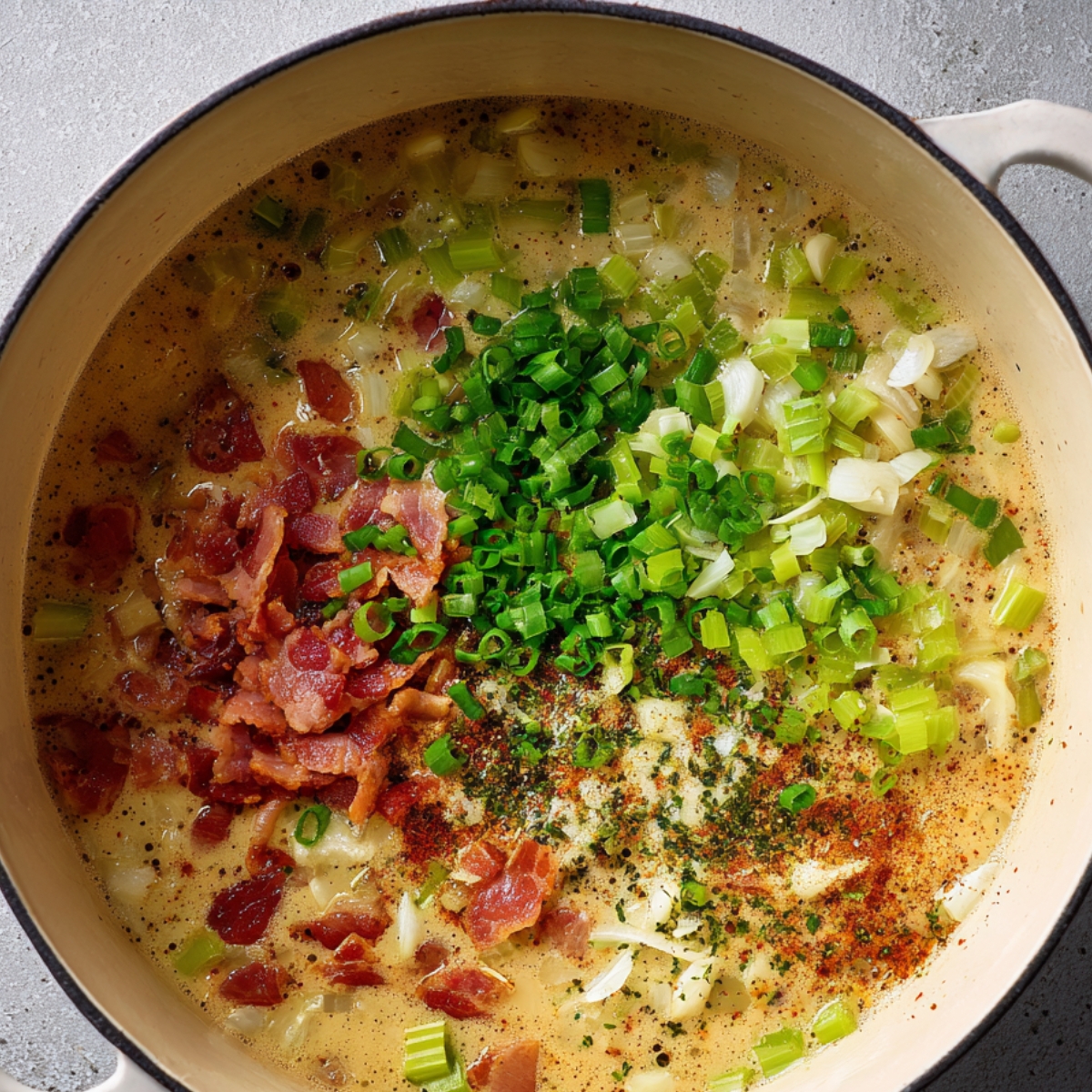 “Sautéed bacon pieces, chopped celery, and green onions cooking in a creamy chowder base in a Dutch oven.”