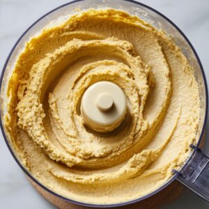 Food processor filled with tahini mixture, chickpeas, garlic, and cumin ready to be blended into hummus.