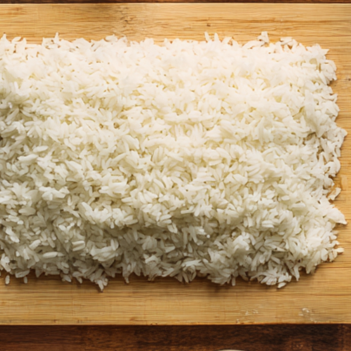 A large pile of freshly cooked rice spread out on a bamboo mat, ready for preparation or serving.