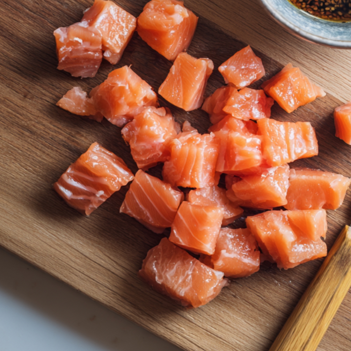 Chopped raw salmon pieces arranged on a wooden board with a small bowl of soy sauce in the background.