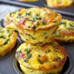 Golden brown baked egg bites muffin tins. with spinach, cheese, and peppers stacked in muffin tins — healthy breakfast idea.”