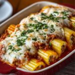 Baked stuffed manicotti topped with melted mozzarella, meat sauce, and fresh parsley in a red casserole dish.”