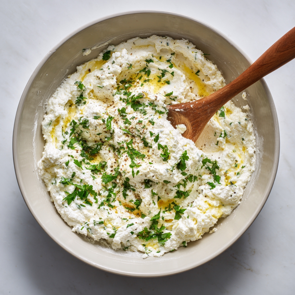 Creamy ricotta cheese filling mixed with parsley, olive oil, salt, and pepper in a bowl with a wooden spoon.”