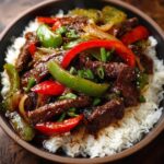 Authentic Chinese pepper steak served over white rice with tender beef strips, red and green bell peppers, and a rich glossy sauce.”