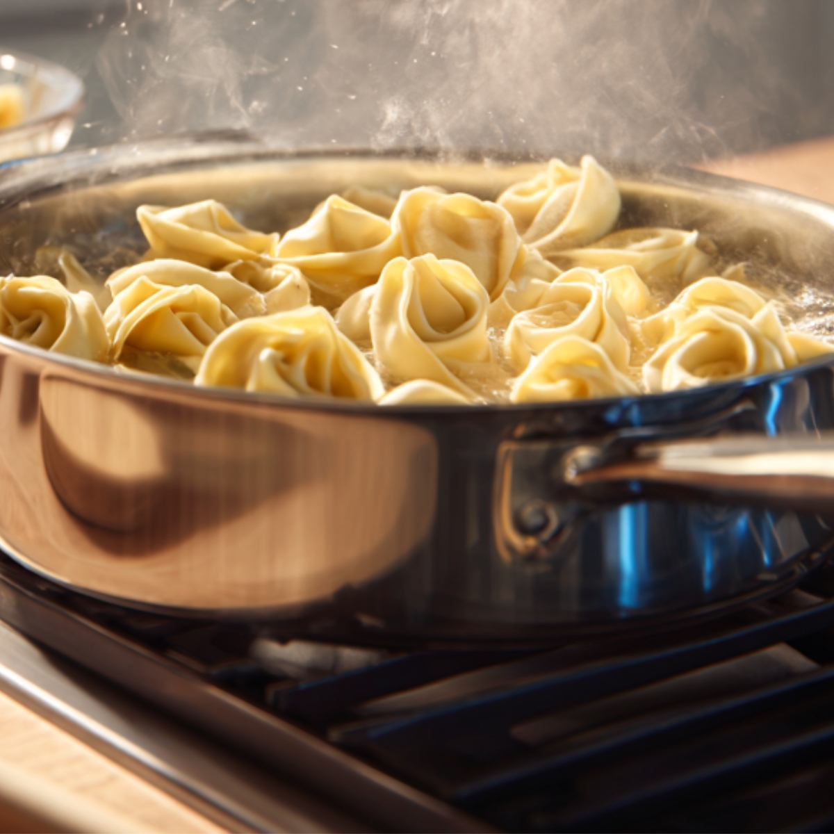 Fresh tortellini boiling in a stainless steel pot on a stove with steam rising from the simmering water.