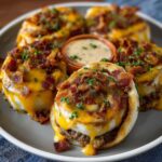 A close-up of cheesy beef and garlic butter bacon cheeseburger rollups topped with melted cheddar and parsley, arranged on a plate with a dipping sauce in the center.