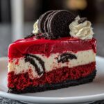 Slice of Red Velvet Oreo Cheesecake Delight with layers of red velvet cake, creamy cheesecake, and cookie pieces, topped with red glaze, whipped cream, and whole Oreo cookies.