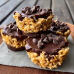 Stack of chocolate peanut butter rice krispie cups topped with chocolate chips, showing layers of peanut butter and chocolate coating.