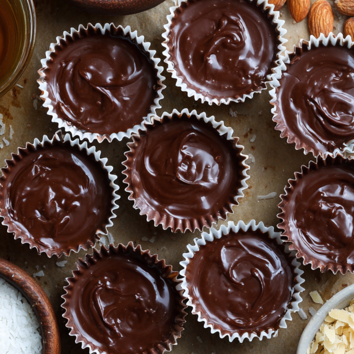 Chocolate peanut butter cups in paper liners, topped with smooth melted chocolate, surrounded by dessert ingredients.