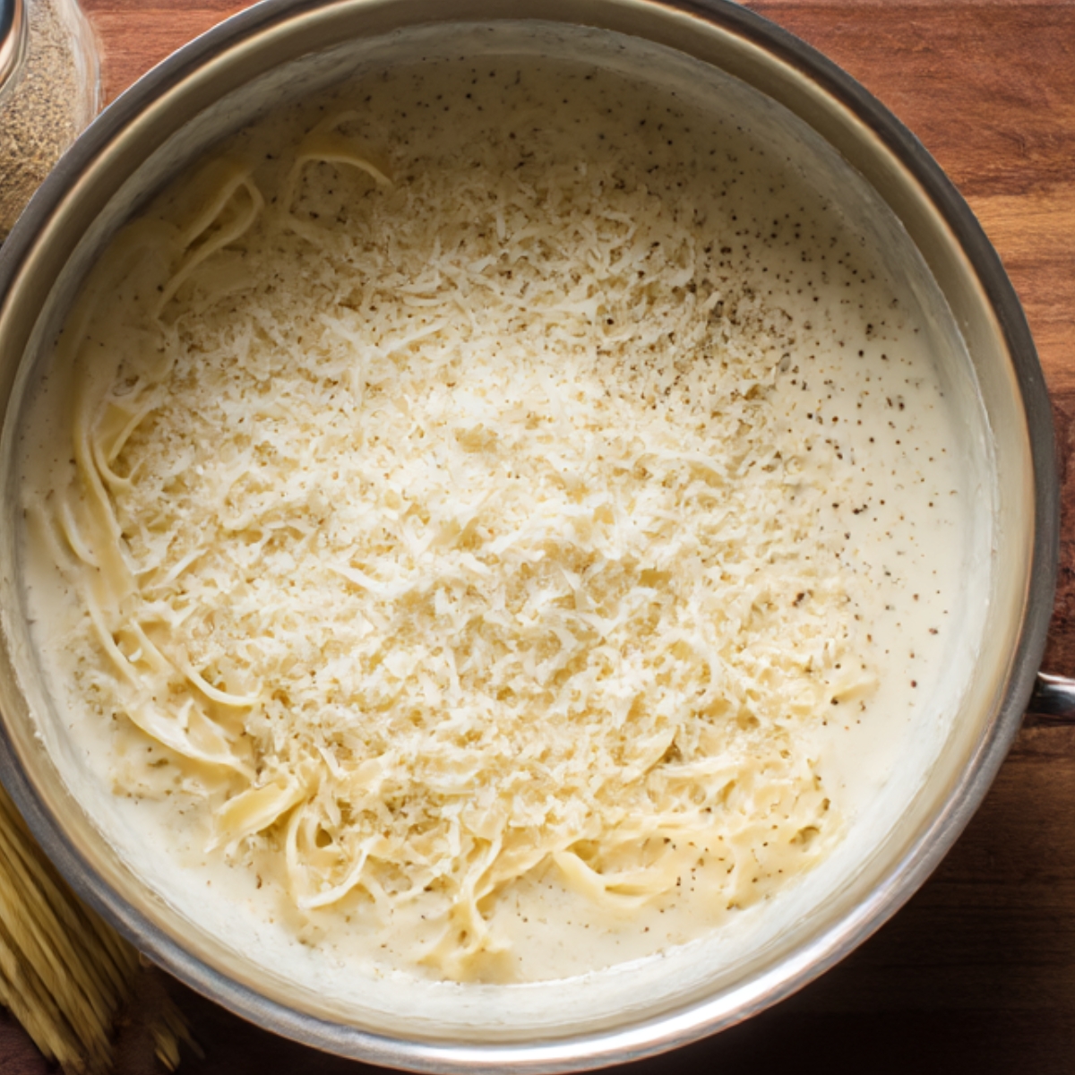 Creamy homemade Alfredo sauce in a saucepan topped with shredded Parmesan cheese and black pepper.