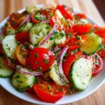 A vibrant cucumber tomato salad with sliced cucumbers, cherry tomatoes, red onions, and chopped herbs tossed in a light vinaigrette.
