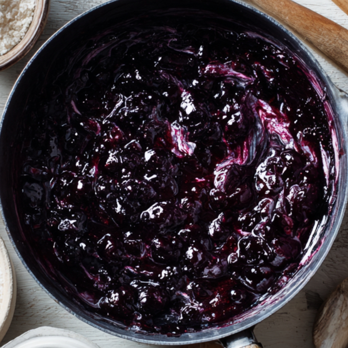 A saucepan of thick, glossy blueberry jam or compote, freshly cooked and ready to use as filling or topping.