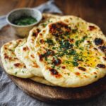 Freshly cooked garlic HOMEMADE naan bread brushed with melted butter and sprinkled with chopped herbs, served on a wooden plate.