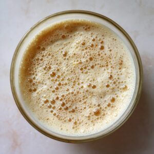 A glass bowl filled with bubbly, activated yeast mixture prepared for making dough.
