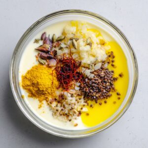 Bowl of yogurt marinade with spices including turmeric, garlic, mustard seeds, and saffron, ready for mixing.