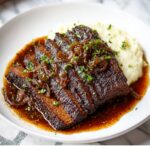 Juicy sliced beef Red Wine Braised Brisket topped with caramelized onions and fresh herbs, served over creamy mashed potatoes with gravy.
