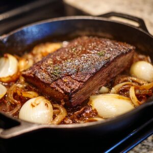 Tender beef brisket roasting in a cast iron skillet with caramelized onions and rich brown gravy.