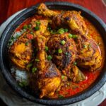 Nigerian chicken-style spicy chicken curry served over steamed white rice in a black bowl, topped with green onions.
