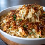 “A baked French onion chicken casserole with golden caramelized onions and melted cheese, being scooped out to show its creamy, cheesy texture.”