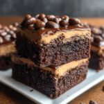 “Two stacked squares of fudgy coffee brownies topped with a creamy mocha frosting and decorated with glossy chocolate-covered coffee beans.”