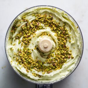 - A bowl of light green pistachio cream or frosting being mixed, topped with chopped pistachios.
