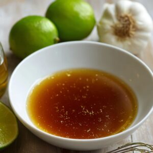 A plate of honey lime chicken served over fluffy rice, topped with caramelized lime slices and fresh chopped herbs. The chicken is coated in a glossy honey-lime glaze with bits of chili and cilantro scattered over it, capturing the perfect balance of sweet, tangy, and spicy flavors.