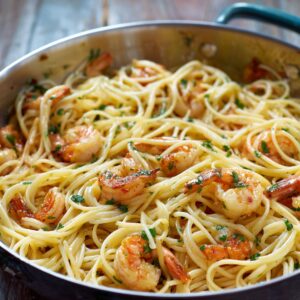 A skillet filled with garlic butter shrimp pasta, featuring tender shrimp and spaghetti tossed in a light, buttery sauce with fresh parsley. The dish glistens with olive oil and golden bits of sautéed garlic.