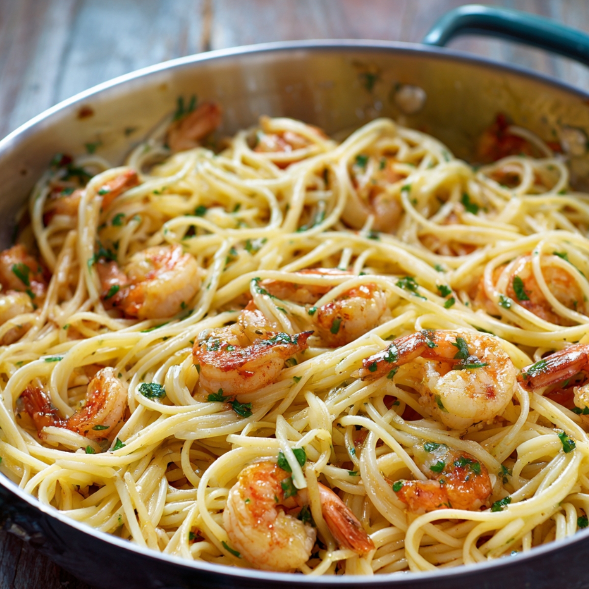 A skillet filled with garlic butter shrimp pasta, featuring tender shrimp and spaghetti tossed in a light, buttery sauce with fresh parsley. The dish glistens with olive oil and golden bits of sautéed garlic.