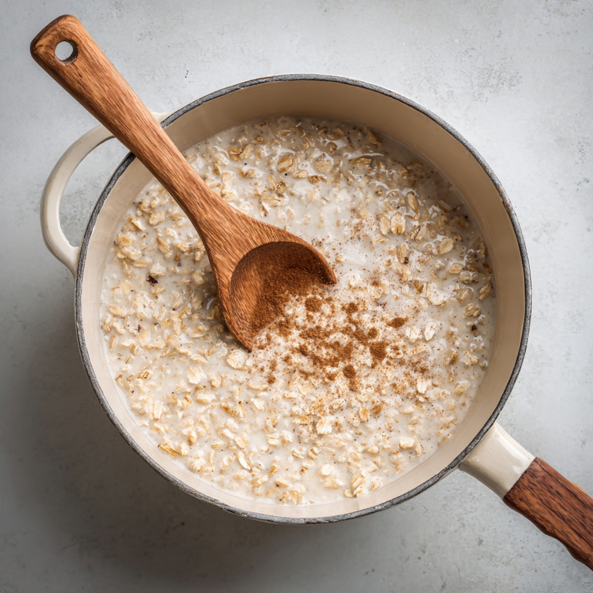 “Pot of warm oatmeal cooking on the stove with cinnamon sprinkled on top and a wooden spoon resting in the mixture.”