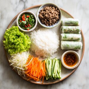 A platter arranged with fresh Vietnamese-style ingredients - rice noodles in the center, ground meat, herbs, lettuce, carrots, cucumbers, bean sprouts, and fresh spring rolls, served with a bowl of dipping sauce.