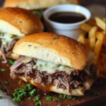 A French dip–style Crock Pot French Dip Sandwiches with shredded beef, melted cheese, and a cup of au jus (dipping sauce).