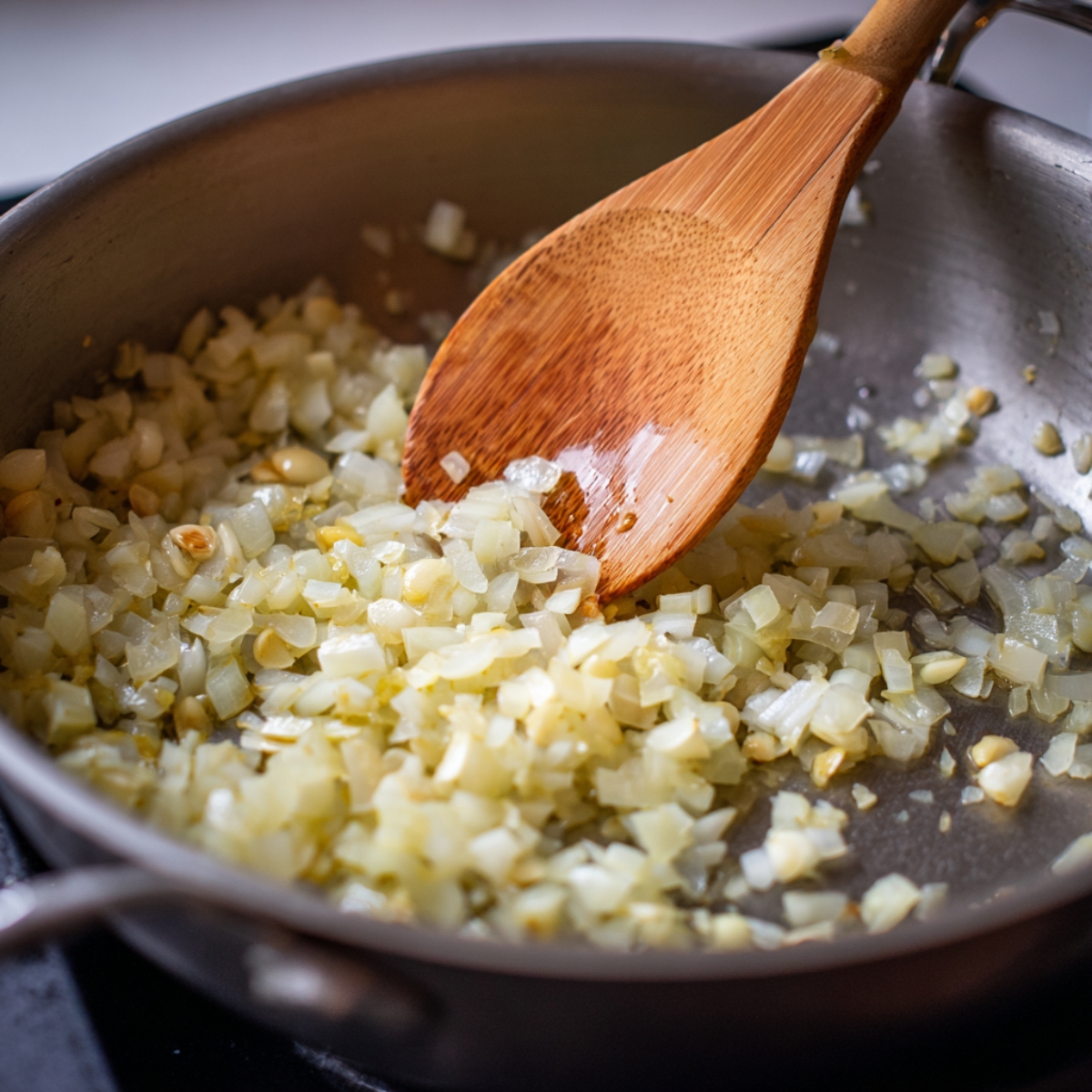“Diced onions and garlic sautéing in a pan with a wooden spoon until soft and golden, creating the flavor base for cauliflower soup.”