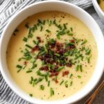 “Bowl of potato leek soup leek soup topped with crispy bacon bits, chopped chives, and cracked black pepper.”